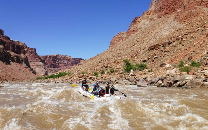A raft is navigated through whitewater, framed by tall canyon walls.